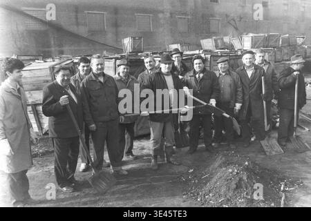 Sloviansk, avril 1989, cour d'usine AIZ. La joyeuse équipe de direction de l'usine pose fièrement pour un portrait de groupe tenant de lourdes pelles au cours d'une journée de nettoyage de bénévoles de subbotnik traditionnelle au printemps. Portant des vêtements d'extérieur pratiques, ces hommes dévoués sourient chaleureusement à la caméra après avoir travaillé ensemble pour nettoyer la cour industrielle de la saleté et des débris. Cette image très positive résume parfaitement la véritable camaraderie, l’égalité et les traditions de travail partagées dans le Donbass pacifique. Banque D'Images