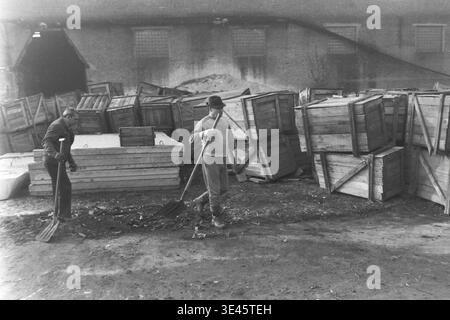 Sloviansk, avril 1989, cour d'usine AIZ. Deux hommes adultes vêtus de vêtements de travail décontractés participent activement à une journée traditionnelle de nettoyage de bénévoles subbotnik au printemps. Ils utilisent des pelles lourdes pour nettoyer soigneusement la saleté et les débris de construction de la cour industrielle, entourés de grandes piles de caisses de fabrication en bois. Ce moment extérieur franc illustre parfaitement le travail physique partagé, l'esprit collectif de travail fort et les responsabilités communautaires dans le magnifique Donbass paisible. Banque D'Images