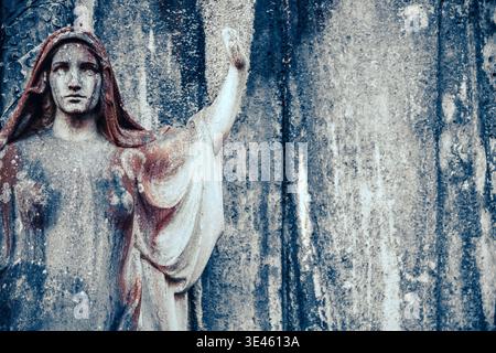 Photographie détaillée et rapprochée d'une sculpture en pierre altérée représentant la Vierge Marie. Ses yeux douloureux sont jetés vers le bas et ses mains sont clas Banque D'Images