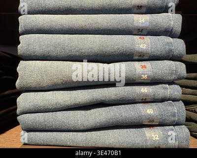 Pile de jeans bleus pliés de différentes tailles dans un magasin de détail avec étiquettes de taille visibles. Photo mobile Banque D'Images