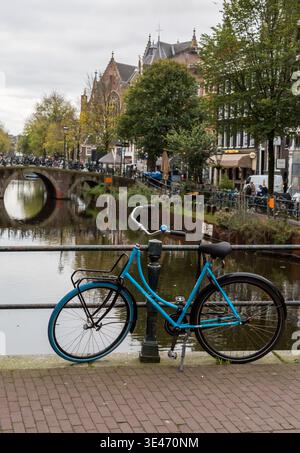 Un vélo bleu appuyé contre des balustrades métalliques sur un pont au-dessus de l'un des canaux d'Amsterdam, avec des arbres d'automne en arrière-plan Banque D'Images