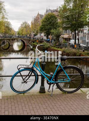 Un vélo bleu appuyé contre des balustrades métalliques sur un pont au-dessus de l'un des canaux d'Amsterdam, avec des arbres d'automne en arrière-plan Banque D'Images