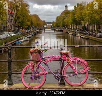 Un vélo rose décoré de fleurs connu sous le nom de « vélo de fleur » appuyé contre des balustrades métalliques sur un pont sur l'un des canaux d'Amsterdam, la Hollande Banque D'Images