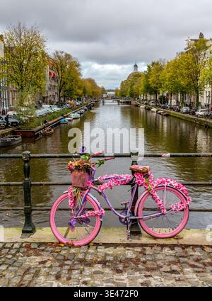 Un vélo rose décoré de fleurs connu sous le nom de « vélo de fleur » appuyé contre des balustrades métalliques sur un pont sur l'un des canaux d'Amsterdam, la Hollande Banque D'Images