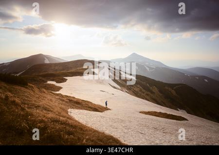 Crête couverte de neige menant vers des sommets montagneux lointains sous la lumière dorée. Sentier de randonnée pittoresque dans les hautes terres avec vue panoramique sur le paysage naturel Banque D'Images