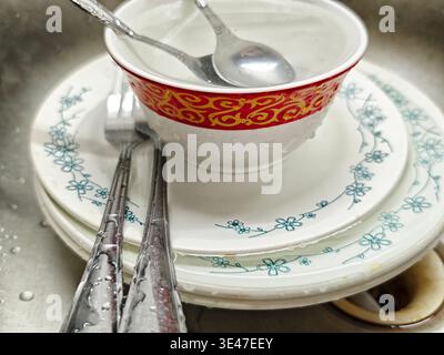 La vaisselle et les ustensiles sont empilés dans un évier. Des gouttelettes d'eau sont visibles sur les articles après le nettoyage d'un repas dans la cuisine. Banque D'Images