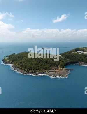 Vue aérienne de la végétation tropicale luxuriante et de la côte rocheuse des îles du Salut avec un navire ancré dans la mer bleue aux îles du Salut, française Banque D'Images