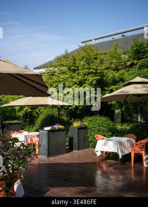 Terrasse extérieure vide du restaurant dotée d'une terrasse en bois, de parasols et de tables à manger recouvertes de tissus blancs entourées d'arbres verdoyants. Banque D'Images