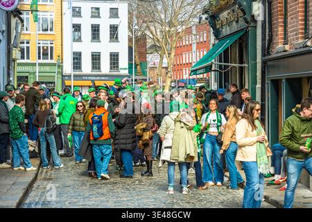 Scène de rue festive avec des gens en tenues vertes et des chapeaux de trèfle pour le festival Patrick’s Day dans la ville de Dublin. Banque D'Images