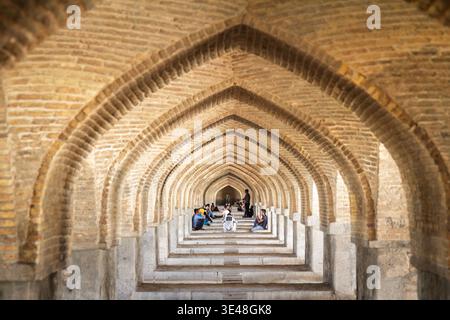 ISPAHAN, IRAN - 7 AOÛT 2016 : de jeunes Iraniens s'assoient et parlent sous les arches répétées du pont Khaju à Ispahan, dans le centre de l'Iran, symbole de l'Iran Banque D'Images