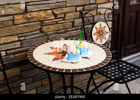 Deux gobelets en papier remplis de délicieuses cuillères à crème glacée assis sur une table dans un café d'été en plein air. Concept rafraîchissant de nourriture de rue avec backgr flou Banque D'Images