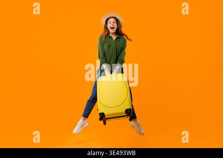 Femme saute avec une valise jaune sur fond orange vif dans une scène animée Banque D'Images