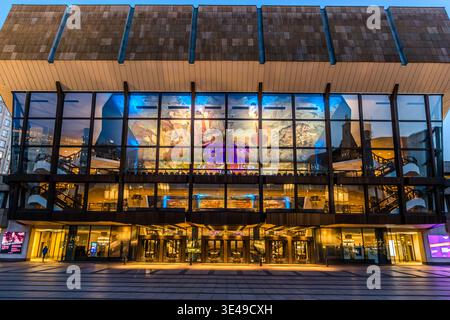 Gewandhaus de Leipzig au crépuscule : la façade vitrée illuminée de la salle de concert révèle la peinture à grande échelle du plafond dans le hall ; la zone d’entrée est parsemée de quelques visiteurs. Leipzig, Saxe, Allemagne Banque D'Images