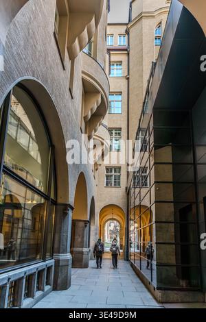 Une vue à travers un passage étroit avec des arcades courbes et des éléments de verre modernes ; deux personnes marchent vers la sortie éclairée. Leipzig, Saxe, Allemagne Banque D'Images