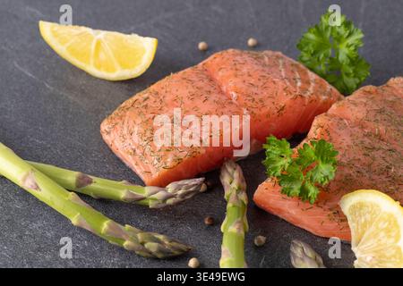Steaks de saumon crus avec asperges vertes, tranches de citron et épices sur une planche de pierre. Banque D'Images