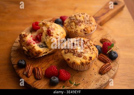 Délicieux muffins aux baies et aux noix de pécan servis sur une planche de bois rustique avec des fruits frais Banque D'Images