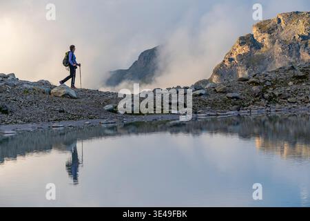 Une personne se tient sur un terrain rocheux, regardant un lac de montagne turquoise magnifique entouré. Habillé en équipement de randonnée et tenant des bâtons de trekking. Wildsee Banque D'Images
