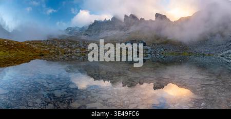La brume se lève au-dessus d'un lac paisible Wildsee dans les montagnes Pizol au lever du soleil, jetant une atmosphère mystique. Le terrain rocheux et les eaux claires reflètent le Banque D'Images