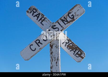 vieux panneau de passage à niveau en bois avec peinture blanche écaillée et fond de ciel bleu Banque D'Images