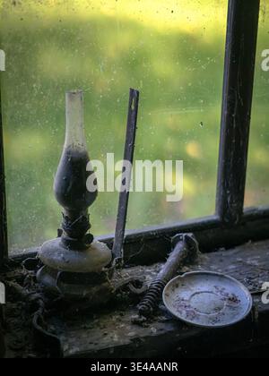 Lampe à huile poussiéreuse sur un rebord de fenêtre sale dans une maison abandonnée Banque D'Images