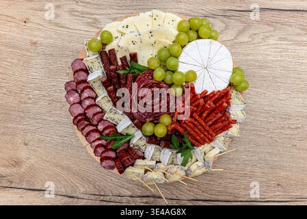 Plateau rond de fromage en bois présentant diverses charcuteries, fromages et raisins verts Banque D'Images