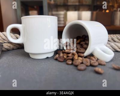 grains de café torréfiés frais renversant d'une petite tasse blanche sur une table sombre avec de la corde. Banque D'Images