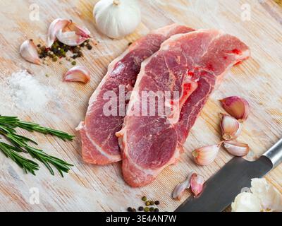 Gros plan de l'épaule de filet de porc cru avec de l'ail et du romarin Banque D'Images