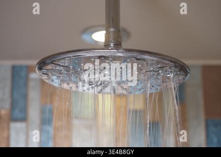L'eau coule de pomme de douche ronde dans la salle de bains moderne Banque D'Images