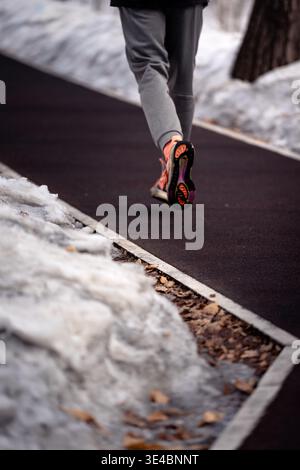 Un coureur en tenue athlétique brillante fait du jogging le long d'un chemin dégagé entouré de neige hivernale Banque D'Images
