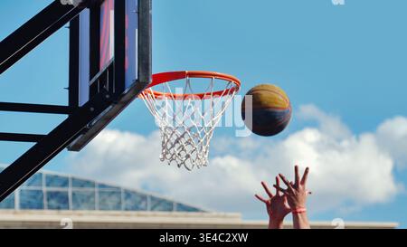 Plan d'action d'un ballon de basket-ball volant vers un cerceau avec les mains du joueur levées. Banque D'Images