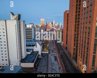 Une perspective surélevée regardant le long d'une ligne de chemin de fer vers les gratte-ciel de la ville de Manchester tandis que la première lumière de l'aube illumine les bâtiments. Banque D'Images