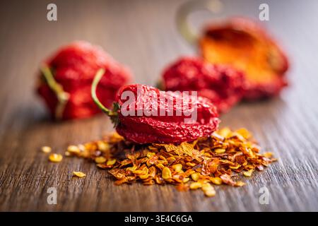 Gros plan de piments rouges séchés et de flocons de piments rouges écrasés dispersés sur une surface en bois, mettant en évidence la couleur vive, la texture froissée et fier Banque D'Images