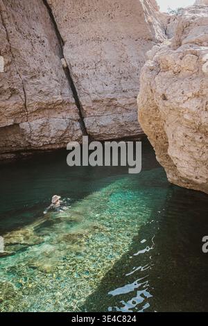 Homme dans le chapeau nageant dans la belle eau claire de l'oued à Oman Banque D'Images