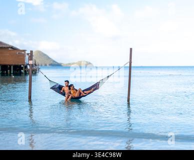 Un couple profite d'un après-midi serein se prélasser ensemble dans un hamac au-dessus des eaux calmes. Un couple multiethnique diversifié d'une femme asiatique et d'un homme caucasien en vacances de luxe Banque D'Images