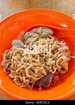 Plan rapproché et en grand angle d'un bol de nouilles sèches servies dans un bol orange vif, avec nouilles aux œufs bouclés, porc char siu, boulettes de poisson, etc Banque D'Images