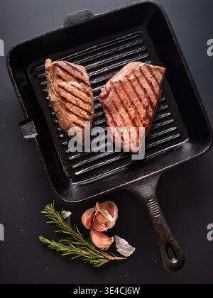 Deux morceaux de flanc de rôti de bœuf grillé et de croupe sont assis sur une poêle en fonte. Les herbes fraîches et l'ail sont placés à côté de la poêle. La scène capt Banque D'Images