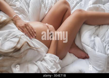 Femme enceinte allongée sur le lit avec les mains caressant son ventre enceinte Banque D'Images