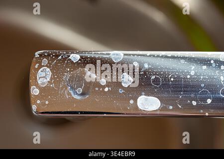 Gros plan de calcaire blanc séché et de taches d'eau sur une surface chromée brillante de poignée de robinet de salle de bains ou de cuisine Banque D'Images
