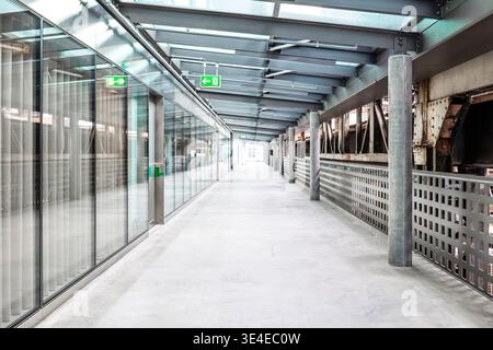 Passerelle industrielle moderne avec murs de verre, poutres en acier et sol en béton dans un bureau lumineux ou un bâtiment public. Vue grand angle, lumière naturelle, no p Banque D'Images