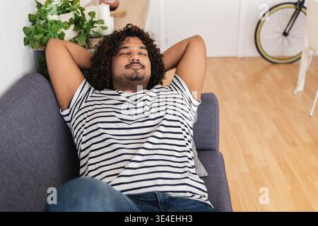 Jeune homme indien se reposant sur un canapé à la maison Banque D'Images