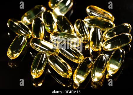 Capsules d'oméga 3 doré sur fond réfléchissant noir, macro gros plan de suppléments d'huile de poisson brillant pour une utilisation dans les soins de santé Banque D'Images