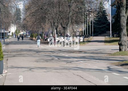 Les visiteurs se promènent et font du vélo le long d'un sentier ensoleillé chaud dans le parc de la ville. Ukraine, Kiev, Expocenter of Ukraine, 27 mars 2026 Banque D'Images