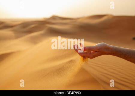 Gros plan de la main laissant couler le sable dans le vent dans le désert d'Abu Dhabi, eau. Textures désertiques, éléments naturels, voyages, aventures et paysages du moyen-Orient c Banque D'Images