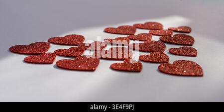 Formes de coeur rouge scintillantes dispersées sur fond blanc, amour romantique et concept de la Saint-Valentin avec espace de copie Banque D'Images