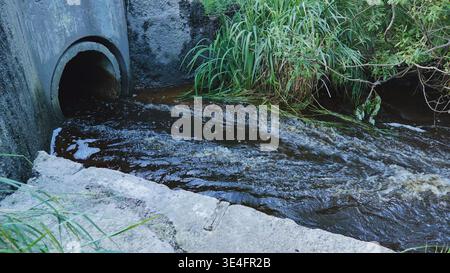 Eaux usées polluées se déversant d'un tuyau en béton dans une rivière sombre et turbulente Banque D'Images