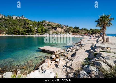 Une vue panoramique grand angle de la plage de Kasjuni à Split, Croatie. Le cliché comprend une jetée en bois, une rive rocheuse et une mer Adriatique turquoise cristalline Banque D'Images