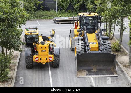 Deux véhicules de construction JCB jaunes stationnés sur une route asphaltée bordée d'arbres. Londres, Royaume-Uni, 14 juillet 2024 Banque D'Images