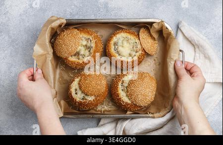 Nourriture, dans les mains des femmes plaque de cuisson avec Julienne dans des petits pains au sésame. Petit pain cuit au four avec fromage, champignons, poulet et sauce béchamel. Délicieux homem Banque D'Images