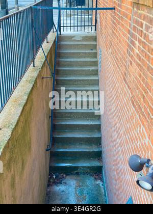 Des escaliers en béton descendent d'un mur de briques brunes à un chemin en dessous. Une balustrade longe les escaliers. La scène se déroule dans une zone urbaine avec un cle Banque D'Images