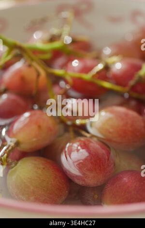 Raisins frais dans un bol avec de l'eau sur la table de cuisine Banque D'Images